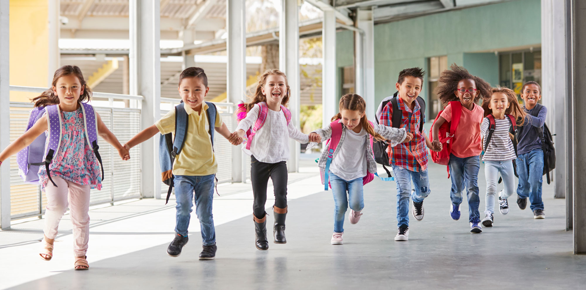 Group of smiling elementary students holding hands and running together down the hallway